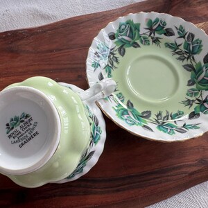 May include: A green and white teacup and saucer set with a floral design. The saucer has a scalloped edge and the teacup has a floral design with the words "Royal Albert Bone China England Lakeside Series Grasmere" on the bottom.