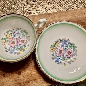 May include: A vintage teacup and saucer set with a green rim and floral design. The floral design features pink, yellow, and blue flowers.