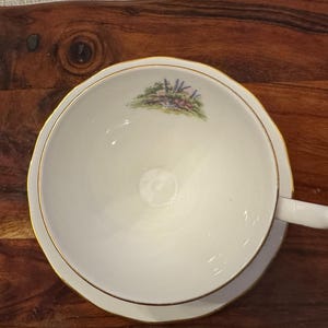 May include: A white teacup with a gold rim and a floral design. The cup is on a wooden surface.