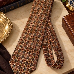 May include: A necktie featuring a repeating geometric pattern of small, interconnected floral-like shapes in shades of brown, tan, black, and cream. The fabric has a textured appearance, and the tie is folded to display its length and width.