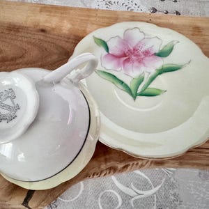 以下が含まれることがあります： 花柄の白いティーカップとソーサーのセット。ソーサーには、ピンクと白の花と緑の葉が描かれています。ティーカップの底には黒い線があり、ソーサーにはスカラップエッジがあります。ティーカップには「Haffers Japan」と表示されています。