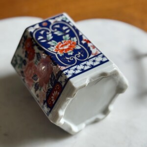 Peut inclure: Un vase en c&eacute;ramique &agrave; base hexagonale et &agrave; motif floral. Le vase pr&eacute;sente un motif bleu et blanc avec des fleurs rouges et roses. Le haut du vase pr&eacute;sente un motif bleu avec une fleur rouge au centre.
