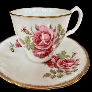 Pu&ograve; includere: Un set da t&egrave; bianco con bordo dorato e un motivo floreale di rose rosa e foglie verdi.