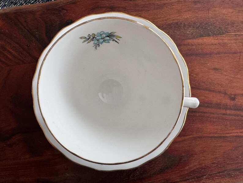 May include: A white porcelain teacup and saucer with a gold rim and a delicate blue floral design.