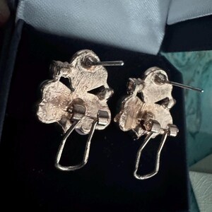 Op de afbeelding: Een paar vintage goudkleurige oorbellen. Elke oorbel heeft een bloemenontwerp met een pin en een scharnierende clipsluiting. De oorbellen zitten in een zwarte sieradendoos.