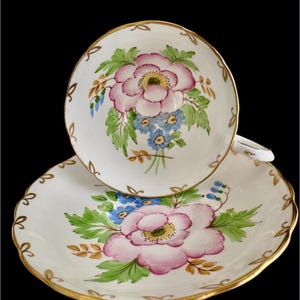 May include: A white teacup and saucer with a pink and blue floral design. The cup and saucer have a gold trim.