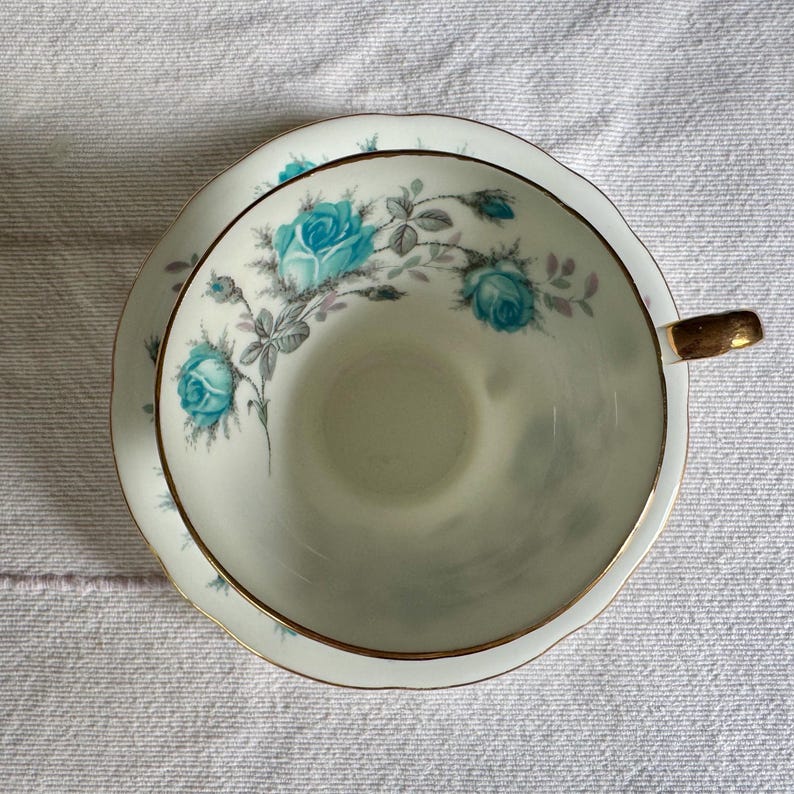 Peut inclure: Un service &agrave; th&eacute; vintage. La tasse et la soucoupe en porcelaine blanche pr&eacute;sentent un motif floral de roses turquoise avec des feuilles grises et une bordure dor&eacute;e. La tasse a une anse dor&eacute;e.