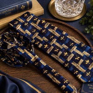 May include: A necktie featuring a dark blue and gold plaid pattern with small yellow leaf motifs. The tie is laid out on a wooden surface, showing a folded section and a long blade. The fabric has a textured appearance with a repeating grid design.