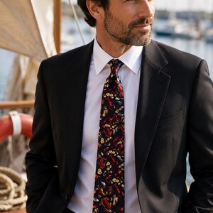 Puede incluir: Una chaqueta de traje negra sobre una camisa blanca y una corbata oscura con un patr&oacute;n repetitivo de langostas rojas, cangrejos y rodajas de lim&oacute;n amarillas. La corbata tiene un acabado liso y est&aacute; atada con un nudo est&aacute;ndar al cuello.