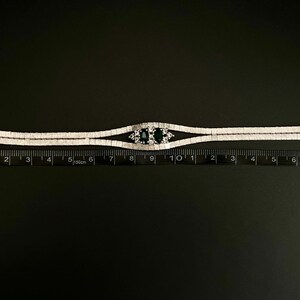 May include: A silver bracelet with a double row of clear stones and a centre piece with two dark blue stones. The bracelet is measured on a ruler, showing it is about 7 inches long.