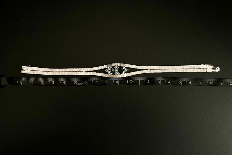 May include: A silver bracelet with a double row of clear stones and a centre piece with two dark blue stones. The bracelet is measured on a ruler, showing it is about 7 inches long.