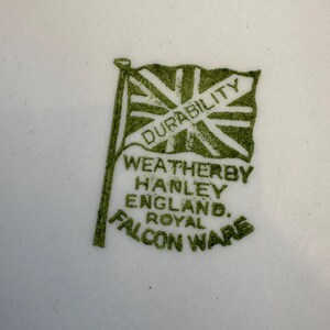 May include: Close-up of a white surface with a green emblem. The emblem features a flag with the word "DURABILITY" and the text "WEATHERBY HANLEY ENGLAND. ROYAL FALCON WARE."