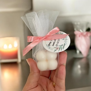 May include: A small white favour bag with a pink ribbon and a round tag that says "Baby Y Gender Reveal 03.08.20."