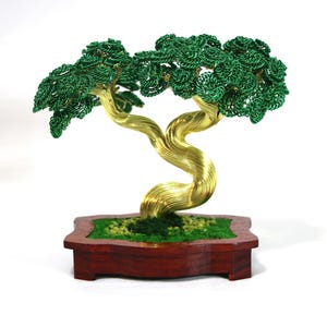 Könnte beinhalten: Handgefertigte Bonsai-Baum-Skulptur. Der Baum hat einen gedrehten, goldfarbenen Drahtstamm und leuchtend grüne Drahtblätter. Er steht in einem dunkelbraunen Holztopf mit grünem Moos.