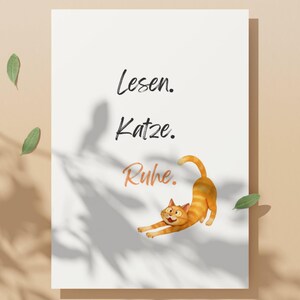 May include: A white rectangular print with a cartoon orange tabby cat stretching. The print has the words "Lesen. Katze. Ruhe." in black and orange script. Green leaves and shadows are in the background.