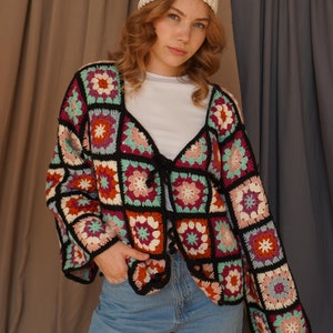 Puede incluir: Una mujer con un cárdigan de ganchillo de colores con una diadema de ganchillo blanca y pantalones vaqueros azules.