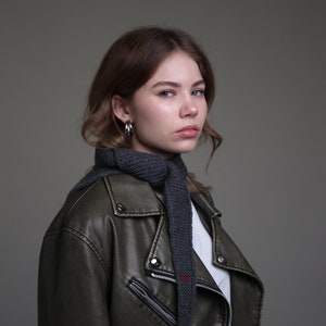 May include: A woman with long brown hair wearing a dark green leather jacket with a gray knitted scarf.