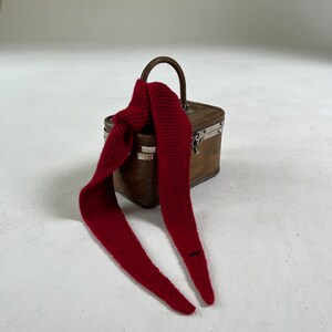 May include: A small wooden box with a metal clasp and a red knitted scarf wrapped around the handle.