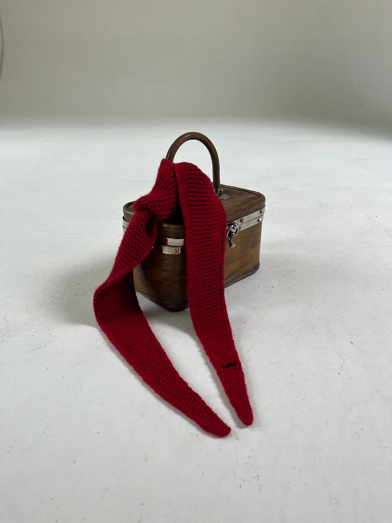 May include: A small wooden box with a metal clasp and a red knitted scarf wrapped around the handle.