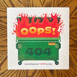 May include: A square print featuring a green dumpster engulfed in flames. The word "OOPS!" is in large orange and red letters above the dumpster. The number "404" is on the dumpster, with the text "Something went SUPER wrong." below.