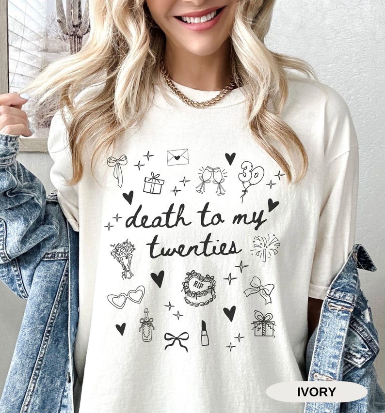 May include: White t-shirt with a black graphic that says "death to my twenties" surrounded by small black illustrations of hearts, gifts, balloons, glasses, lipstick, and other celebratory items. The text "IVORY" is in the bottom right corner.