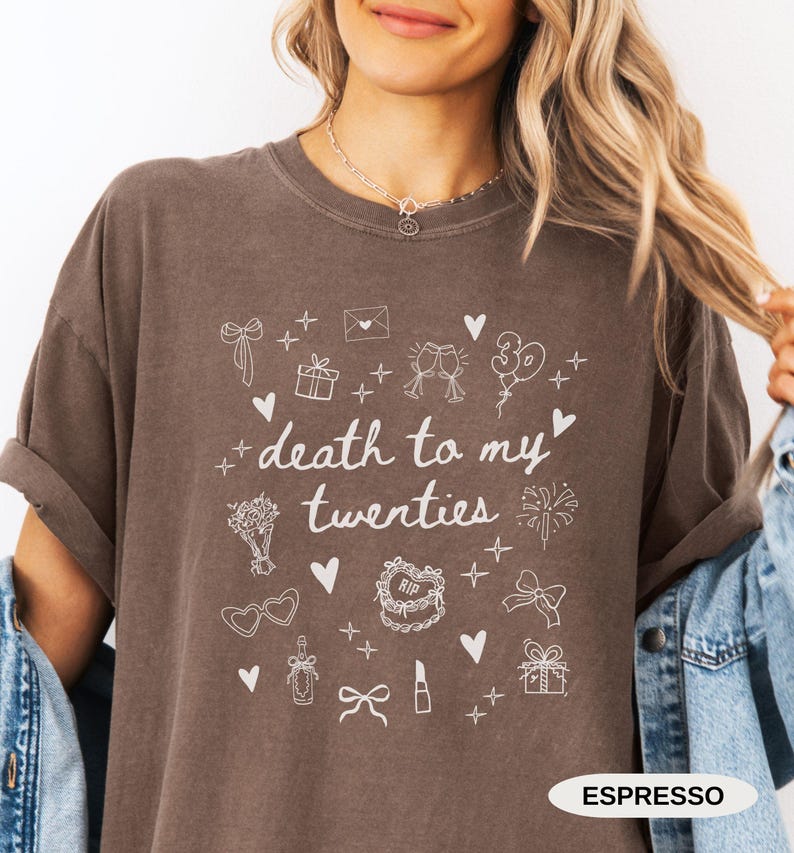 May include: A brown t-shirt with a white graphic that says "death to my twenties" and is surrounded by various white icons, including a gift box, a champagne flute, a lipstick, a bow, and a cake. The text "ESPRESSO" is printed in white at the bottom of the shirt.