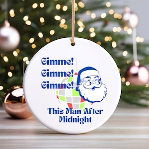 Puede incluir: Adorno de Navidad de cerámica blanca con una ilustración azul y blanca de Papá Noel con una bola de discoteca y el texto "Gimme! Gimme! Gimme! This Man After Midnight".