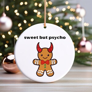 May include: White ceramic Christmas ornament with a gingerbread man wearing red devil horns and a red bow tie. The text "sweet but psycho" is printed on the ornament.