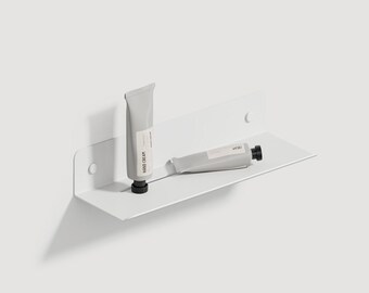 May include: Two white tubes of hand cream on a white metal shelf. The shelf is mounted to a white wall.