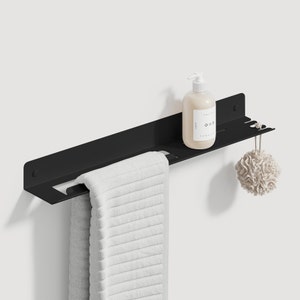 Pode incluir: Prateleira de banheiro de metal preto com uma toalha branca pendurada, uma garrafa de sabonete para as m&atilde;os e uma esponja bege pendurada na lateral.