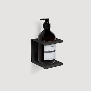 Può includere: Porta sapone da parete in metallo nero con una bottiglia di shampoo in vetro trasparente etichettata "Iberita Shampoo".