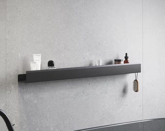 Può includere: Una mensola da bagno in metallo nero montata su una parete grigia, con vari articoli da toeletta. La mensola ha un design minimalista e include articoli come tubetti di lozione, un flacone di profumo e una piccola spazzola.