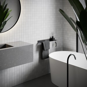 Pode incluir: Um banheiro branco com uma pia de bancada cinza, uma barra de toalha preta com uma toalha cinza, uma banheira branca e uma torneira preta.