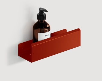 May include: A burnt orange metal shelf mounted on a white wall, holding a brown glass bottle with a black pump dispenser. The bottle has a white label with black text. The shelf is a simple, modern design.