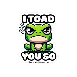 May include: A green cartoon frog with an angry expression sits with its arms crossed. The text "I TOAD YOU SO" is written above the frog and "PunsAndPaws.co" is written below the frog.