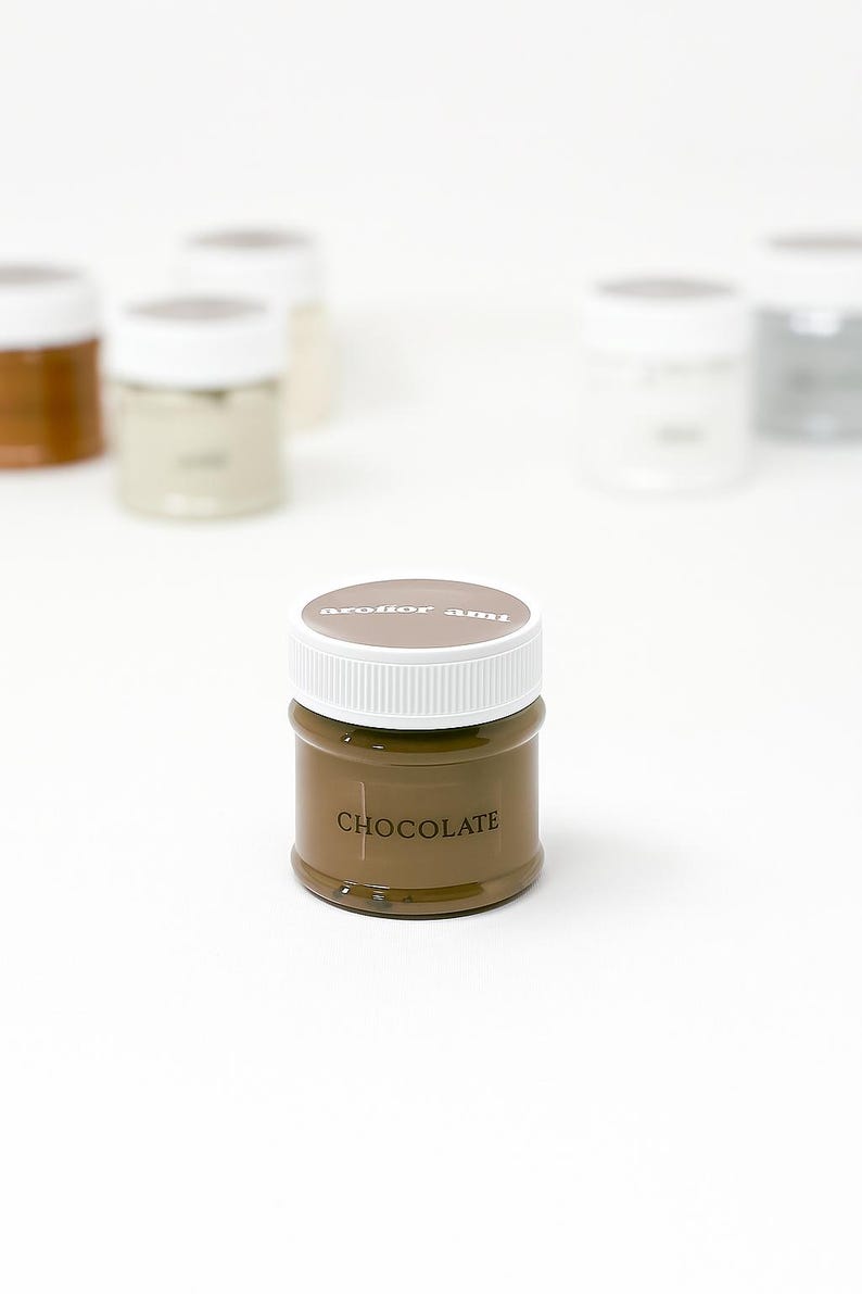 May include: A small, round jar of chocolate-colored paint with a white lid. The word "CHOCOLATE" is printed on the front of the jar. Other jars are visible in the background.