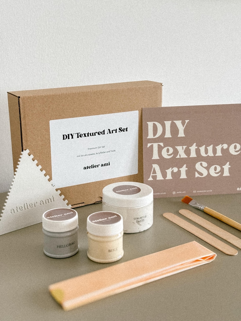 May include: A DIY Textured Art Set with various art supplies. The set includes a cardboard box, containers of paint, a triangular tool, a brush, and wooden sticks. The set is labeled "DIY Textured Art Set" and "atelier ami".
