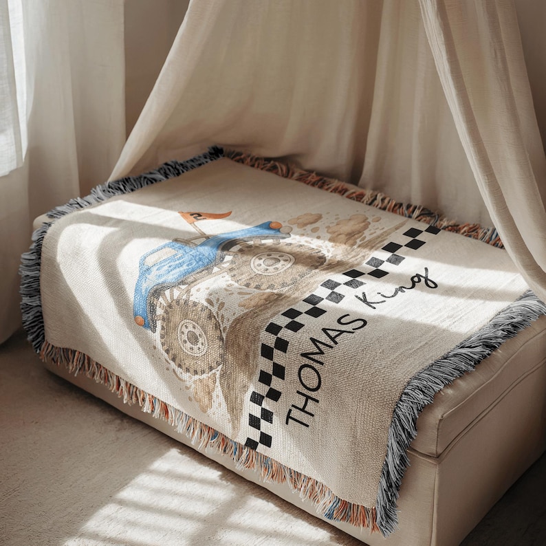Op de afbeelding: Een beige sprei met een blauw tractorontwerp en de naam "Thomas King" in zwart schrift. De sprei heeft een geblokte rand en gefranjerde randen. De tractor heeft grote wielen en een kleine oranje vlag.