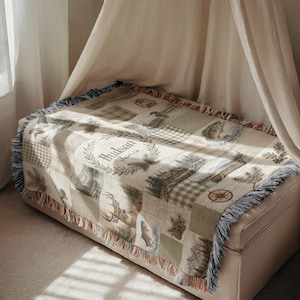K&ouml;nnte beinhalten: Eine gewebte Wohndecke mit Patchwork-Design und Outdoor-Motiven wie Hirsch, Fisch, Tannenzapfen und Kompass. In der Mitte befindet sich ein kreisf&ouml;rmiges Kranzmotiv mit dem personalisierten Text Hudson James in Schreibschrift.