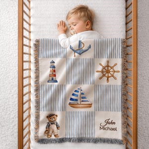 May include: A baby blanket with a nautical theme. The blanket features a blue and white striped pattern with square patches displaying an anchor, lighthouse, ship's wheel, sailboat, and a teddy bear. The name "John Michael" is printed on the blanket.