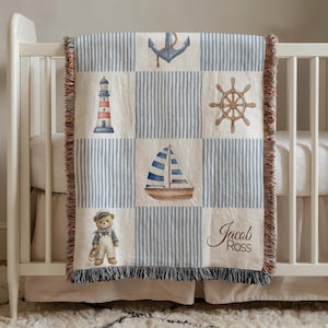 May include: A nautical-themed baby blanket with a blue and white striped pattern and square blocks featuring a lighthouse, anchor, sailboat, and teddy bear. The blanket is personalized with the name "Jacob Ross".
