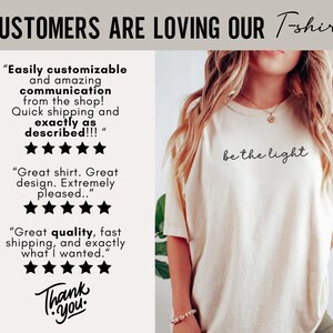 May include: Cream-colored t-shirt with the phrase "be the light" in black script. The image also includes customer reviews and the text "CUSTOMERS ARE LOVING OUR T-shirts". The shirt is part of a clothing line.