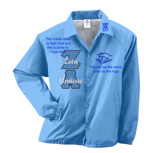 Puede incluir: Chaqueta azul claro con cierre de botones a presión. La chaqueta tiene el texto "Zeta Amicae" en un diseño de dos tonos en la parte delantera. El texto "1948" está en el hombro superior derecho. La chaqueta tiene dos bolsillos delanteros.