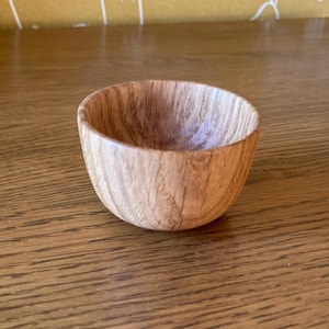 May include: A small, wooden bowl with a natural wood finish. The bowl is round and has a smooth, polished surface.