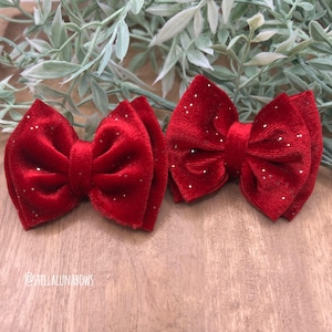 May include: Two red velvet hair bows with glitter. The bows are tied in a double loop and have a sparkly finish.