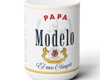 May include: White ceramic mug with a design that resembles a beer can. The design features the words "Papa Modelo" in blue and red lettering, with a gold crest that says "Hecho en Mexico" and "Limited Edition". The text "El mas Chingon" is written in gold lettering below the crest.