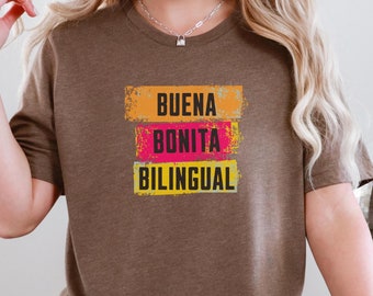 May include: A brown t-shirt with the words "BUENA BONITA BILINGUAL" printed in black on three yellow and orange rectangular blocks with a distressed effect.
