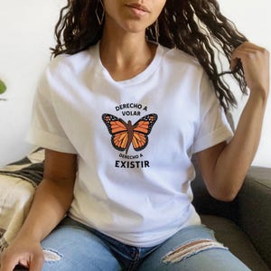 Pu&ograve; includere: T-shirt bianca con un disegno di farfalla monarca arancione e nera. Il testo spagnolo "Derecho a Volar" &egrave; sopra la farfalla e "Derecho a Existir" sotto. La maglietta &egrave; realizzata in materiale morbido.