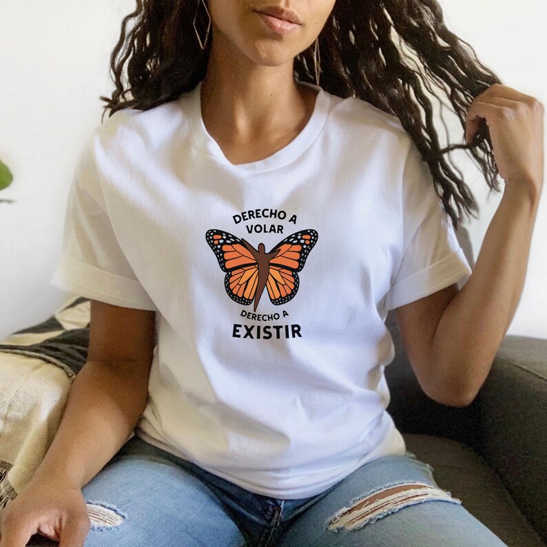 Pu&ograve; includere: T-shirt bianca con un disegno di farfalla monarca arancione e nera. Il testo spagnolo "Derecho a Volar" &egrave; sopra la farfalla e "Derecho a Existir" sotto. La maglietta &egrave; realizzata in materiale morbido.