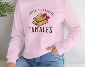 May include: A pink sweatshirt with the text "Santa's Favorite Tamales" and a graphic of tamales tied with a red ribbon.